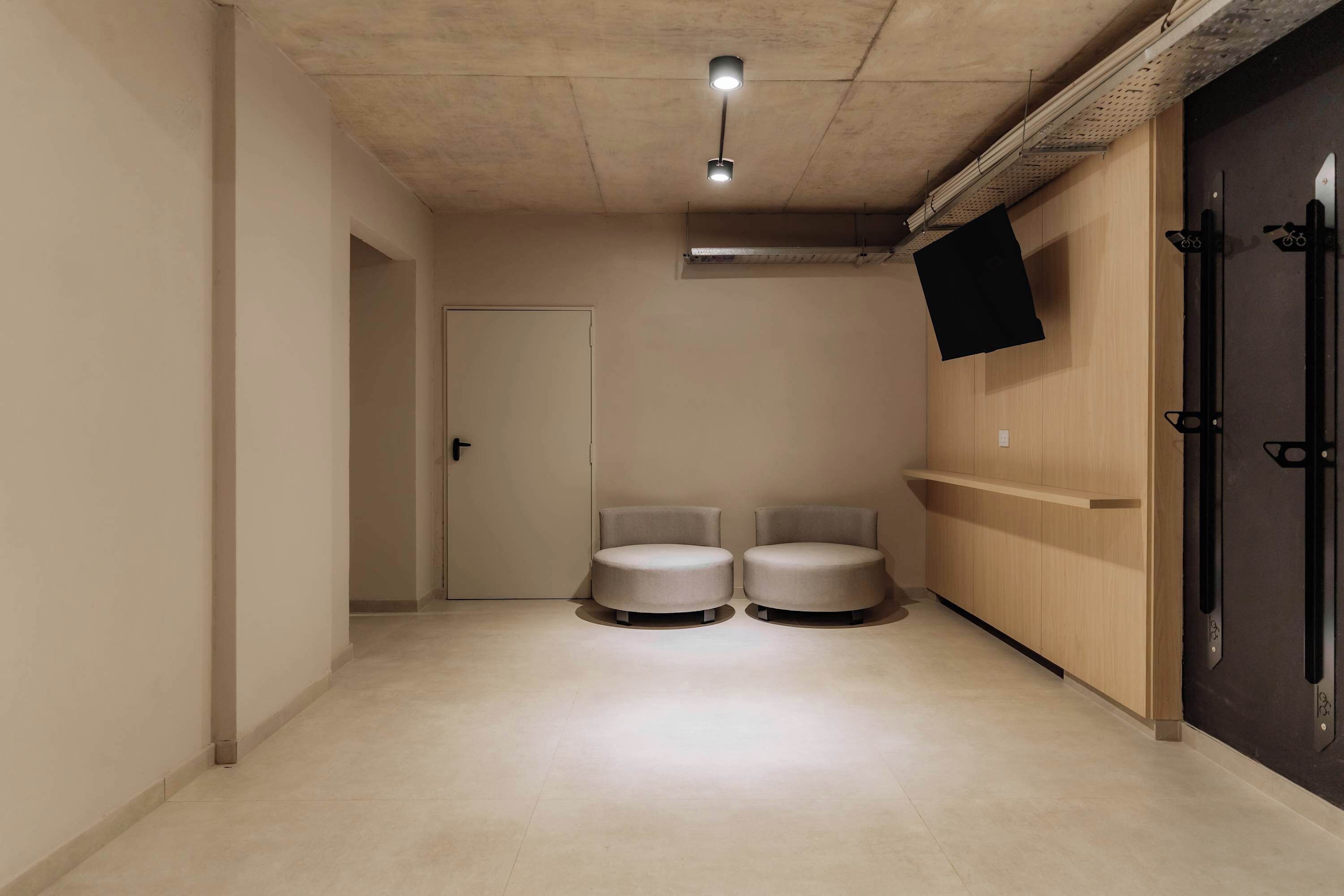 Ein Flur mit zwei runden Sitzbereichen, einer Tür, einem Wand-Fernseher und einem Holzschrank.