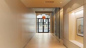 Un pasillo moderno con una puerta de cristal que da a la calle, una lámpara colgante y un cuadro en la pared.