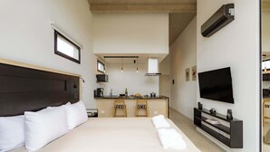 Una habitación de hotel moderna con una cama grande, televisión, kitchenette y vistas a la cocina.