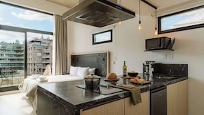Habitación de hotel moderna con una cama grande, kitchenette, vistas de la ciudad y un balcón.