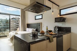 Ein modernes Hotelzimmer mit einem großen Bett, einer Küchenzeile, Blick auf die Stadt und einem Balkon.