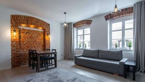 Una sala moderna con chimenea de ladrillo, un sofá gris, una mesa de comedor con sillas y ventanas grandes con cortinas.