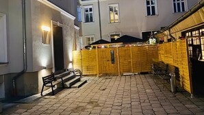 Un patio con valla de madera, un banco y un edificio con entrada iluminada.