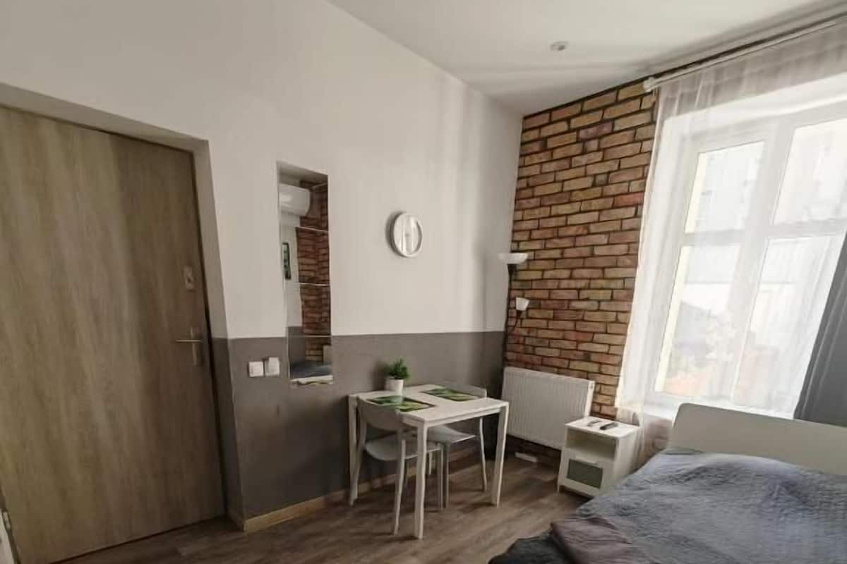 A bedroom with a bed, a desk, a chair, a radiator, and a brick wall.