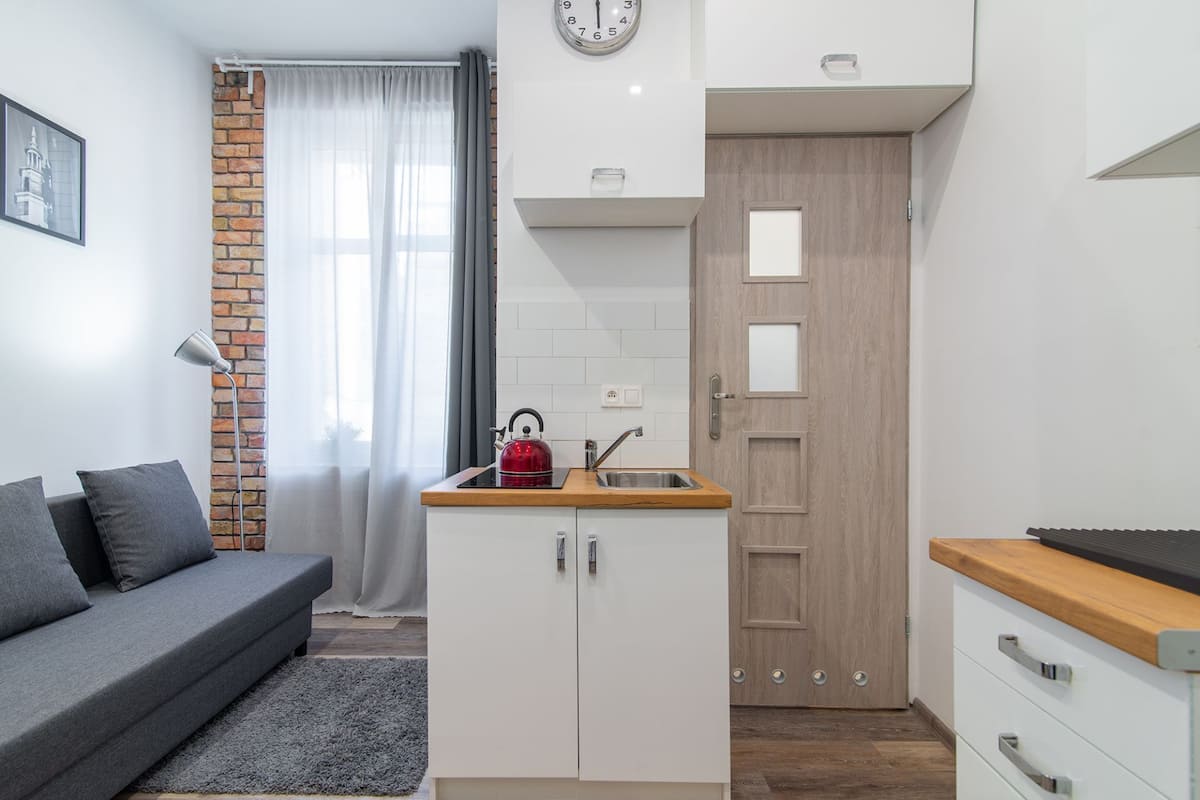 A compact living space with a kitchenette, a sofa, a clock, and a door.