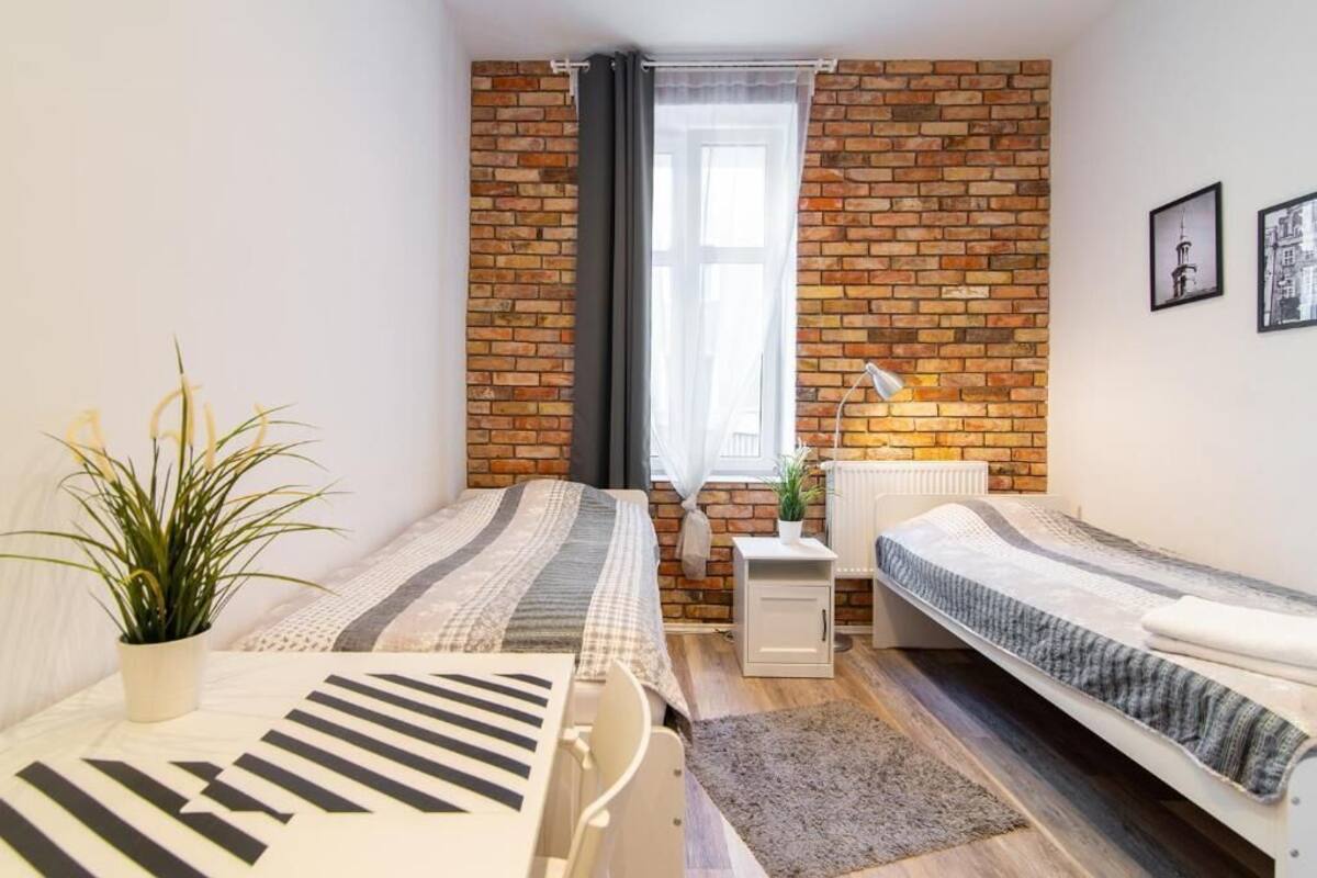 A bedroom with two beds, a radiator, a window with curtains, a plant, and a lamp.