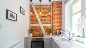 Una cocina con pared de ladrillo, horno empotrado, pileta y ventana con flores.