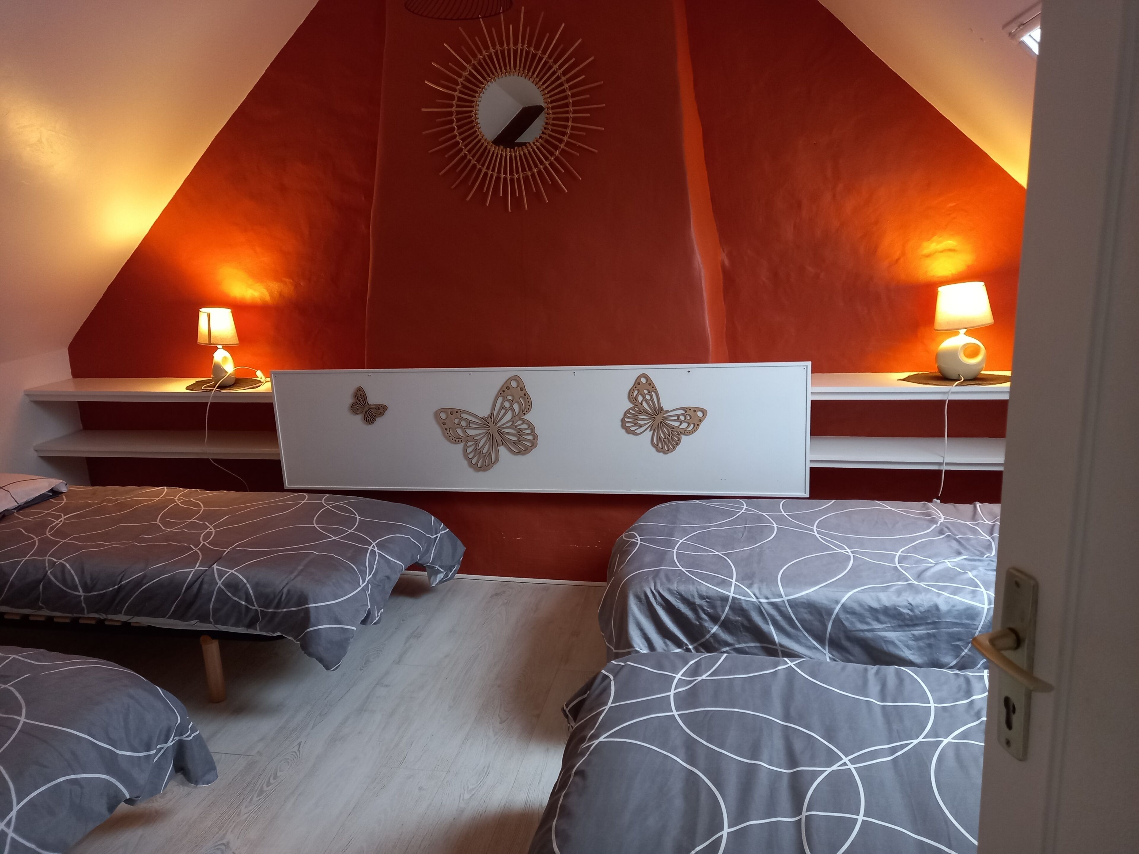Un dormitorio con dos camas, una pared de acento roja, un espejo montado en la pared y lámparas de noche.