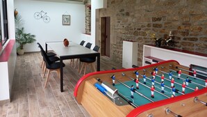 Een kamer met een tafelvoetbaltafel, een eettafel met stoelen, een potplant en een stenen muur.