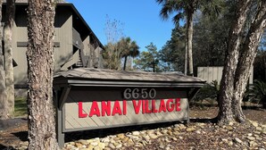 A sign for Lanai Village with a number 6650, surrounded by trees and a gravel path. - Cozy 1-bedroom condo in lovely Diamondhead with AC (Diamondhead)
