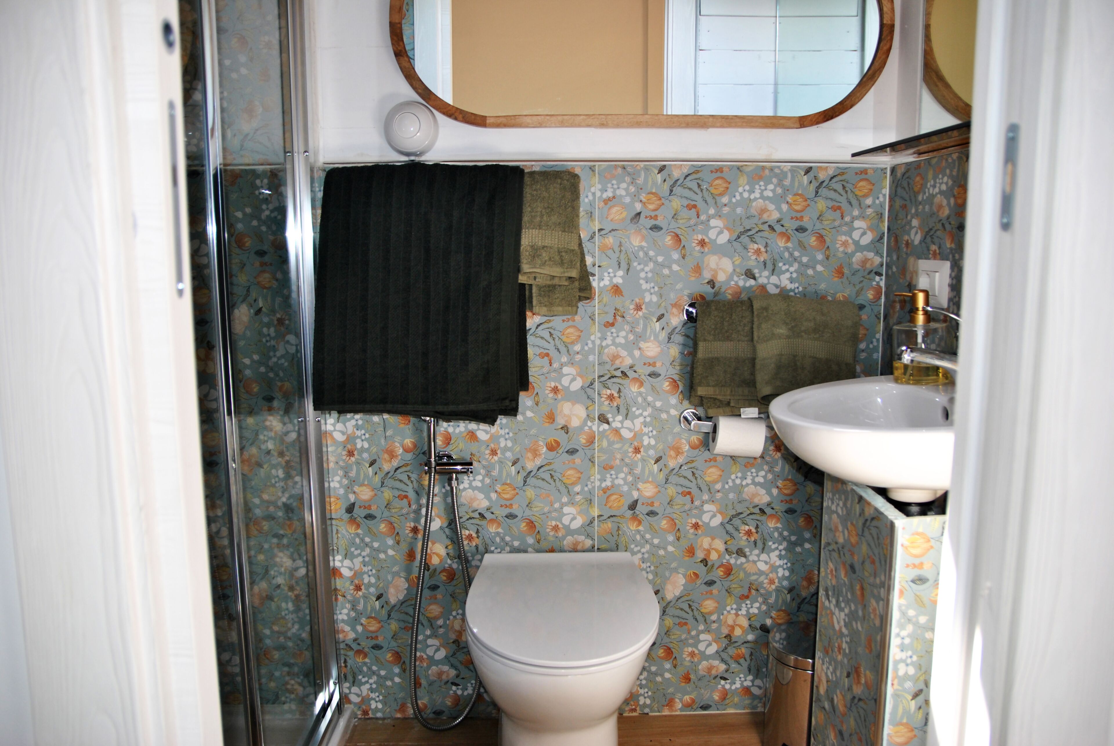 A bathroom with a toilet, sink, shower, and floral-patterned walls.