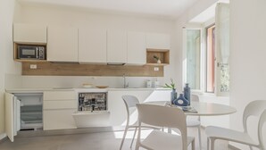 Eine moderne Küche mit weißen Schränken, einer Mikrowelle und einem eingebauten Geschirrspüler. Es gibt einen Essbereich mit weißen Stühlen und einem runden Tisch.