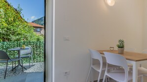 A dining area with a wooden table and white chairs, a potted plant, and a view of a mountain and greenery outside. - Cà Magnolia Appartamento 2 by Varenna Holidays (Lierna)