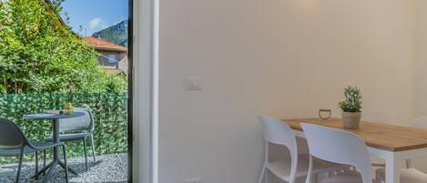 A dining area with a wooden table and white chairs, a potted plant, and a view of a mountain and greenery outside.