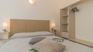A modern bedroom with a bed, bedside lamps, a wooden headboard, a wardrobe, and a magazine on the bed. - Cà Magnolia Appartamento 2 by Varenna Holidays (Lierna)