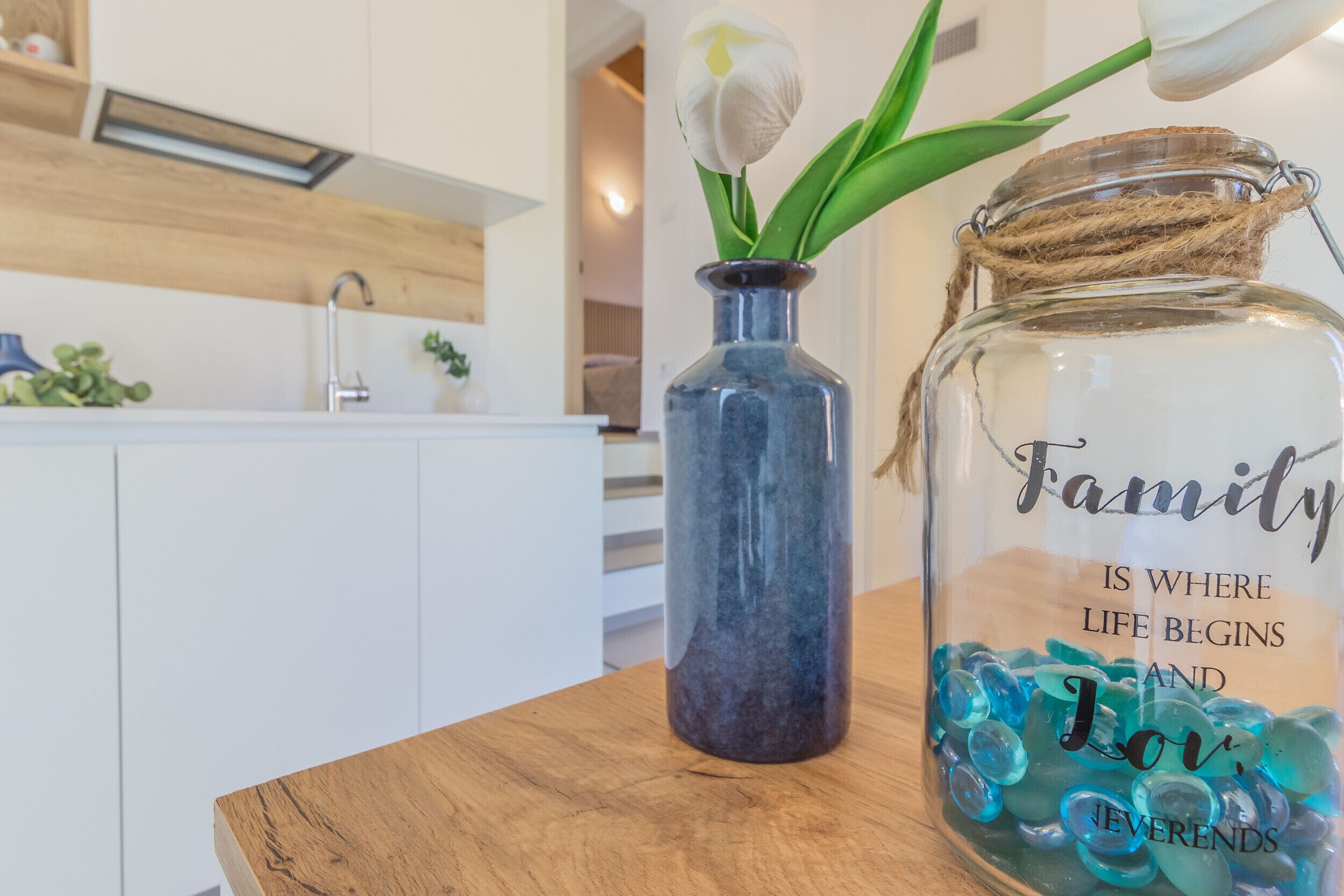 A kitchen counter with a glass jar labeled 'Family is where life begins and love forever ends' and a small vase with a white flower.