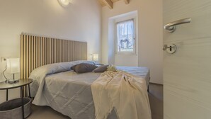 A bedroom with a bed, bedside table, lamp, and a window with curtains. - Cà Magnolia Appartamento 4 by Varenna Holidays (Lierna)