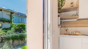 A kitchen with white cabinets, a wooden countertop, and a view of a garden and neighboring buildings. - Cà Magnolia Appartamento 4 by Varenna Holidays (Lierna)