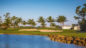 Een golfbaan met zandbunkers, een waterpartij en palmbomen.
