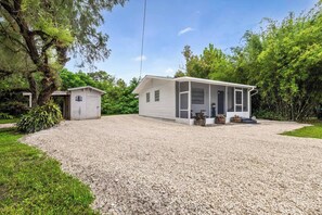 Une maison de plain-pied avec un porche couvert, un petit abri de jardin et une allée gravillonnée.