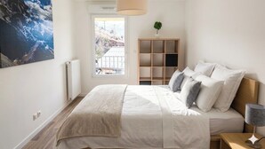 Ein Schlafzimmer mit Bett, Nachttisch, Lampe, Fenster, Heizkörper, Regal und einem Bild.