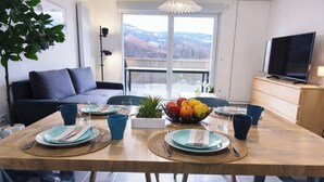 Ein Essbereich mit Tisch für zwei Personen, einer Couch, einem Fernseher und Blick ins Freie.