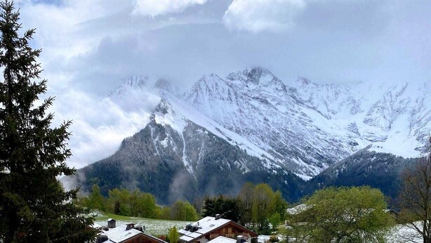 Ein schneebedecktes Feld mit einem Gebäude, das mehrere Fenster und einen Balkon hat, umgeben von Bergen.