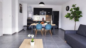 Eine moderne Küche mit schwarzen Schränken, ein Essbereich mit blauen Stühlen und ein graues Sofa.