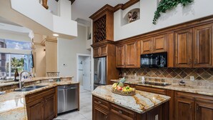 Una cocina con armarios de madera, encimeras de granito, un refrigerador de acero inoxidable y una cesta de frutas en la isla.