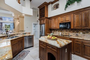 Eine Küche mit Holzausstattung, Granit Arbeitsplatten, einem Edelstahlkühlschrank und einer Obstschale auf der Kücheninsel.