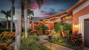Un edificio residencial con fachada de ladrillo, un jardín bien cuidado con diversas plantas y un camino que lleva a la entrada.