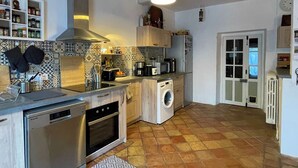 Eine kleine Küche mit Geschirrspüler, Backofen und Waschmaschine, einer gefliesten Spritzschutzwand und einem gemusterten Teppich.