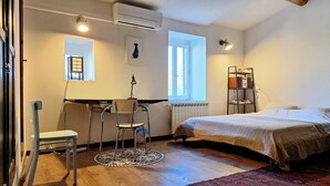 Ein Zimmer mit einem Bett, einem Schreibtisch mit Stuhl, einem Heizkörper, einem Fenster und einem Regal mit Büchern.
