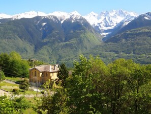 Un paysage montagneux avec des sommets enneigés, un bâtiment jaune doté d’un toit en pente et une forêt verdoyante et dense.