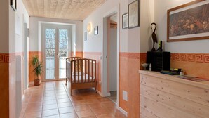 A hallway with a wooden ceiling, a wooden crib, a potted plant, and a reception desk with a framed picture.