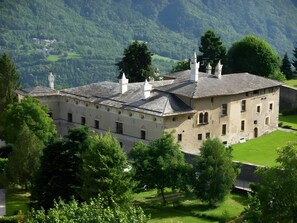Edifici històric amb diverses xemeneies, envoltat de vegetació abundant i un paisatge de muntanyes.
