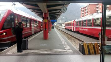 Un quai de gare avec deux trains rouges, une horloge et une personne portant des bagages.