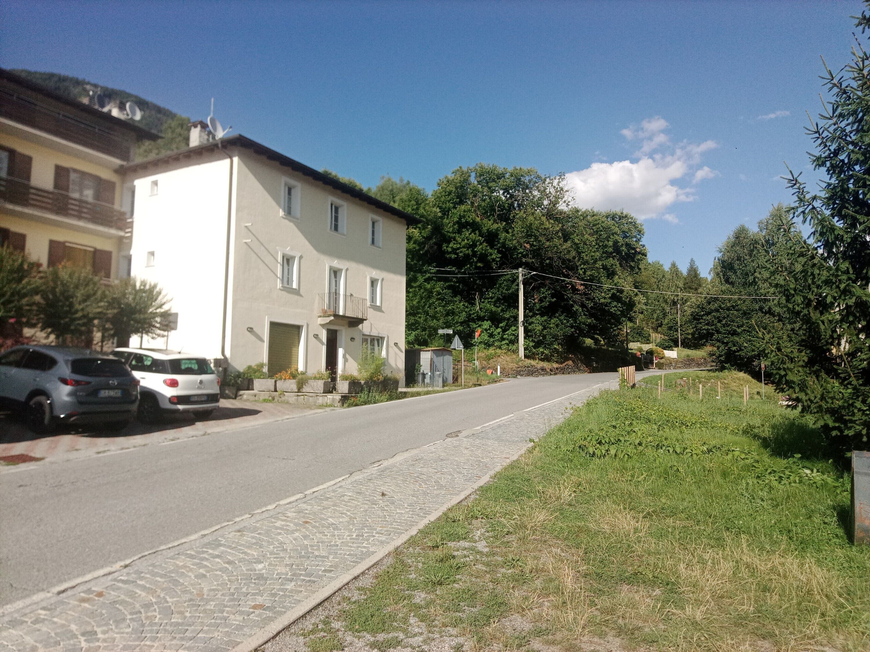 Eine Wohnstraße mit einem zweistöckigen Gebäude, parkenden Autos und einem Kopfsteinpflasterweg.