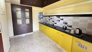 A kitchen with dark wooden cabinets, yellow lower cabinets, a black countertop, and a tiled backsplash. - Thamira Residency (Palayankottai)