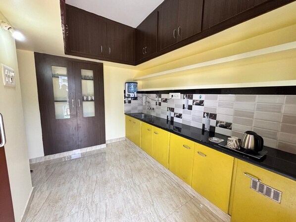 A kitchen with dark wooden cabinets, yellow lower cabinets, a black countertop, and a tiled backsplash. - Thamira Residency (Palayankottai)