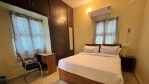 A bedroom with a bed, a desk, a chair, a wardrobe, and an air conditioning unit. - Thamira Residency (Palayankottai)