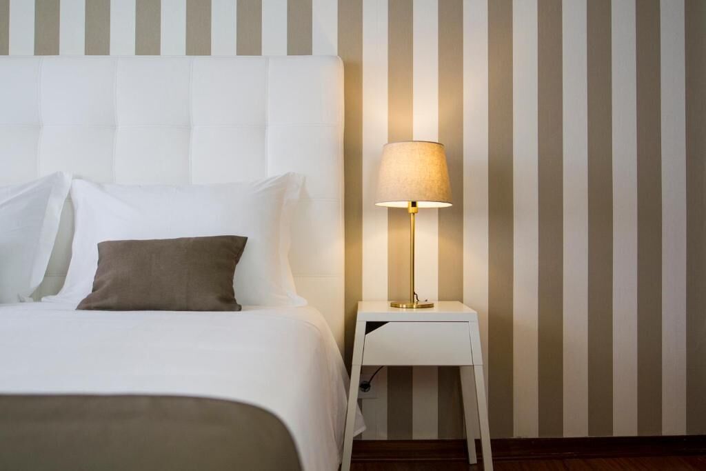 A hotel room with a bed, a nightstand, a lamp, and striped wallpaper.