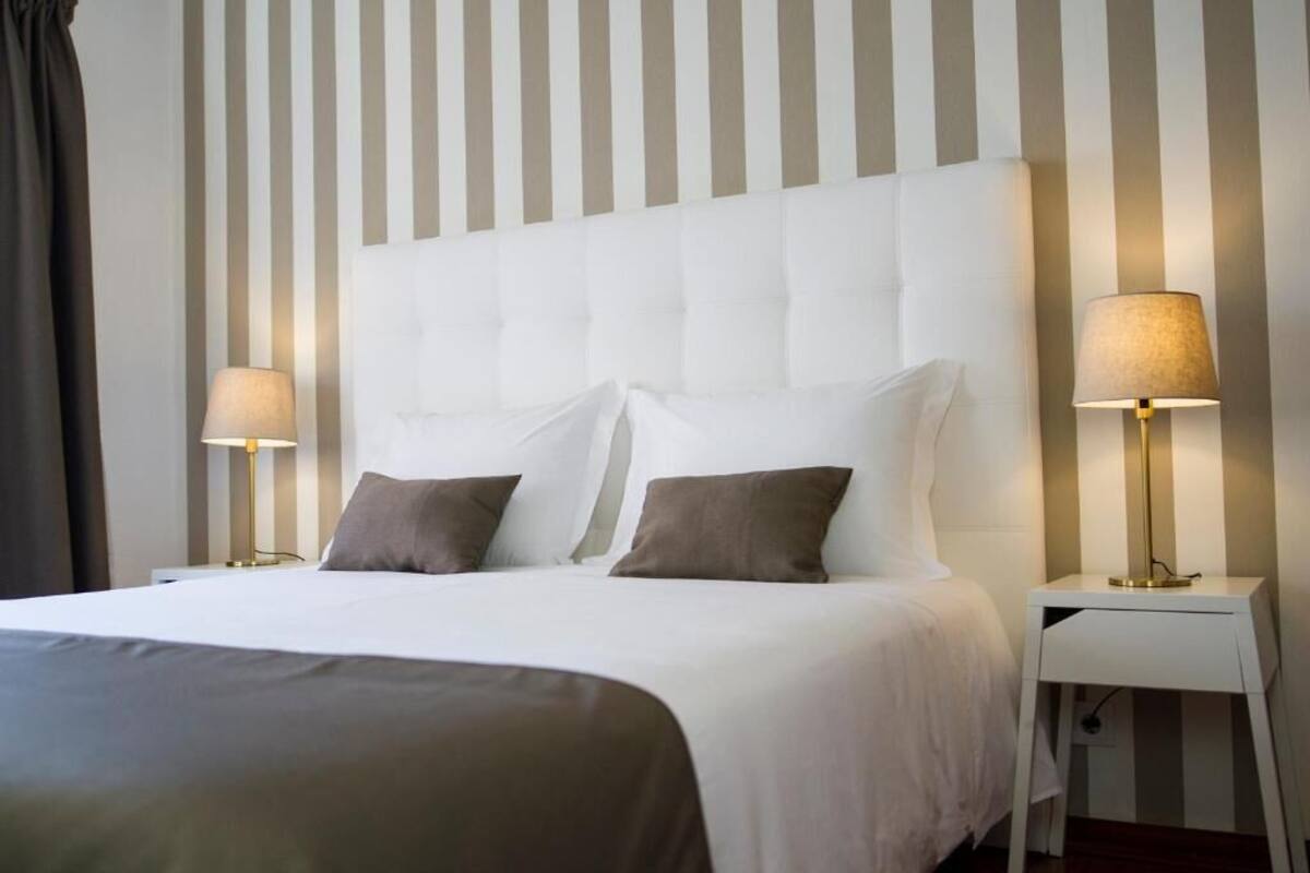Una habitación de hotel con una cama grande, dos lámparas de noche y una pared a rayas.