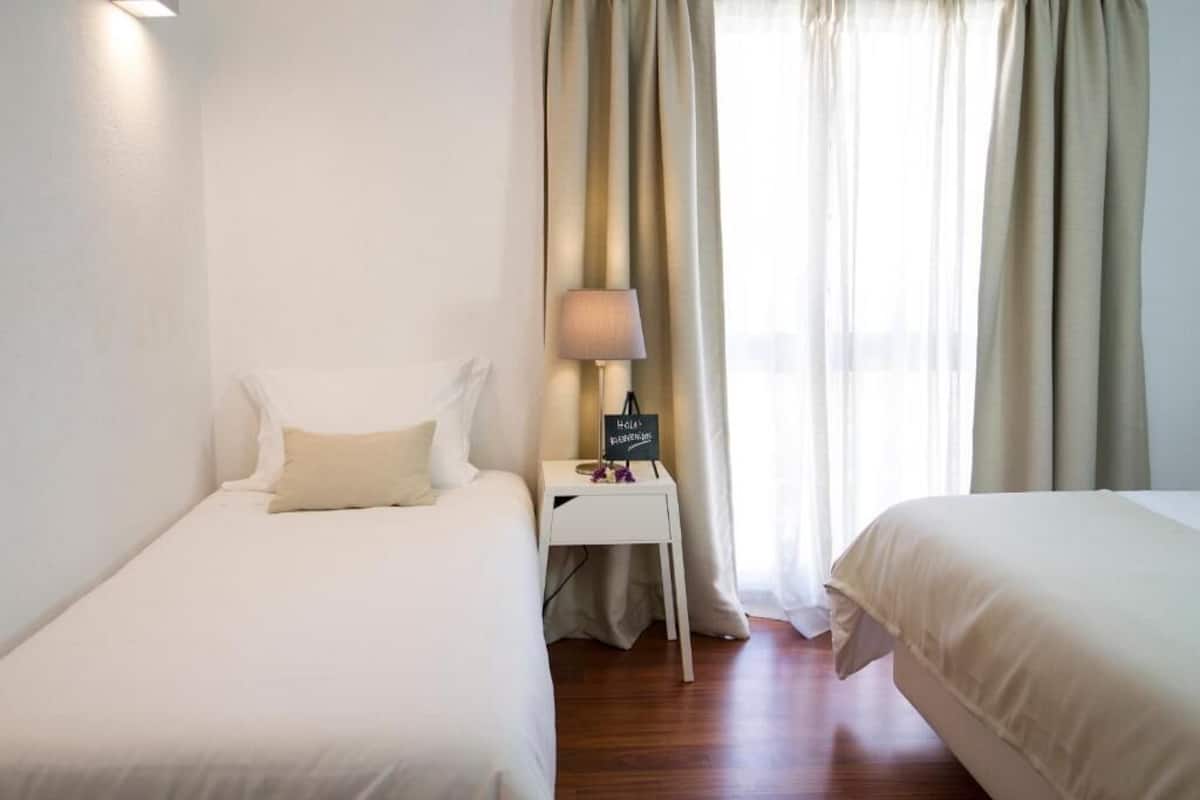 Habitación de hotel con dos camas, una mesita de noche con lámpara, un cartel y una ventana con cortinas.