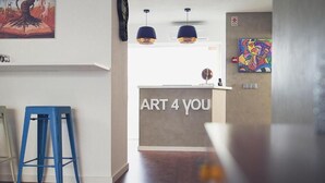 Un mostrador de recepción con letrero 'ART 4 YOU', un taburete azul y obras de arte en las paredes.