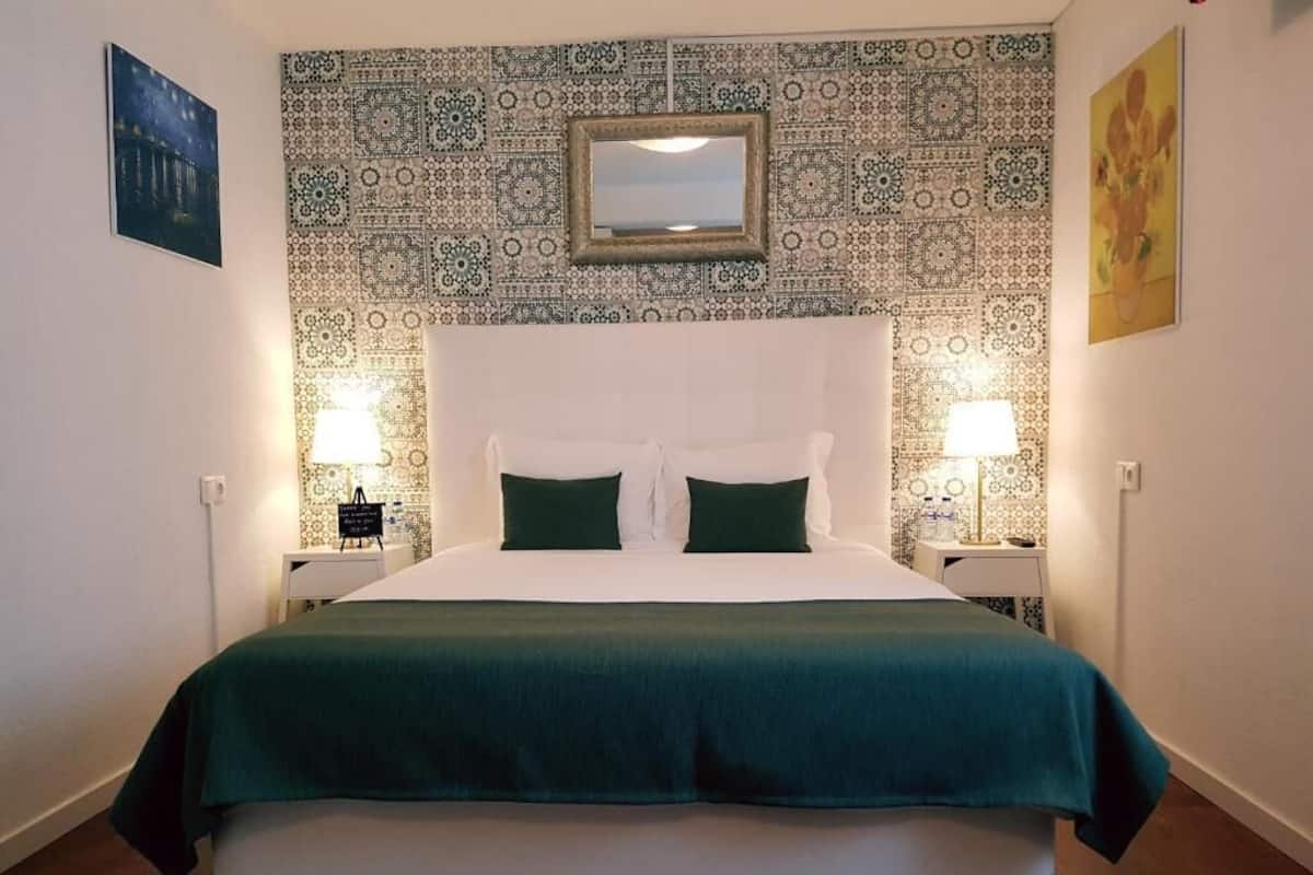 Habitación de hotel con cama, dos lámparas de noche, mesitas de noche, un espejo, papel tapiz estampado y obras de arte en las paredes.