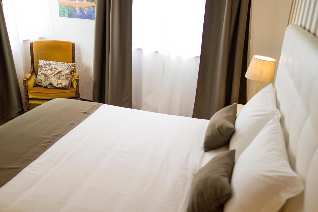 A hotel room with a bed, a chair, a lamp, and curtains.
