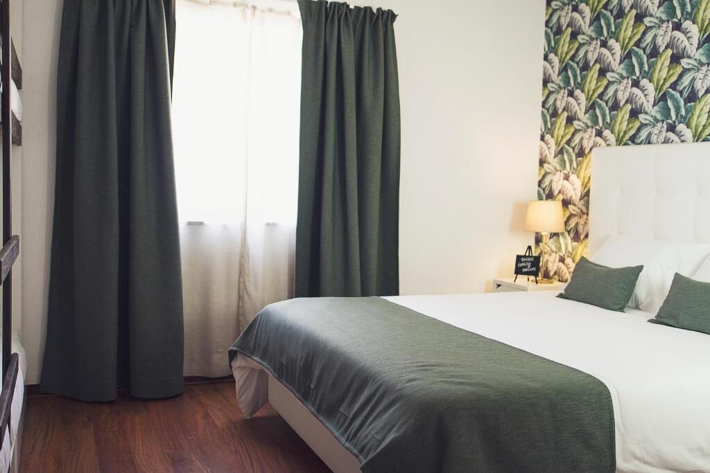 A hotel room with a bed, curtains, a nightstand with a lamp, and a floral wallpaper.