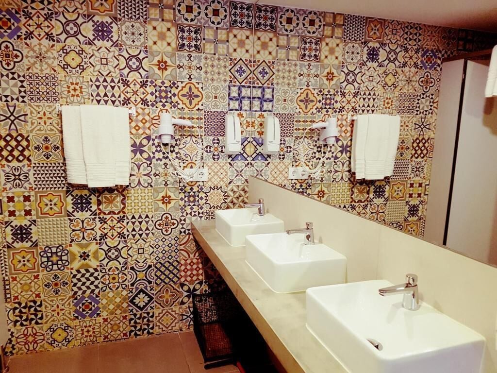 Un baño con pared de azulejos, tres lavamanos y dos dispensadores de toallas.