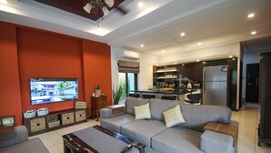 Een moderne woonkamer met een grijze bank, een houten salontafel en een flatscreen televisie aan de muur.